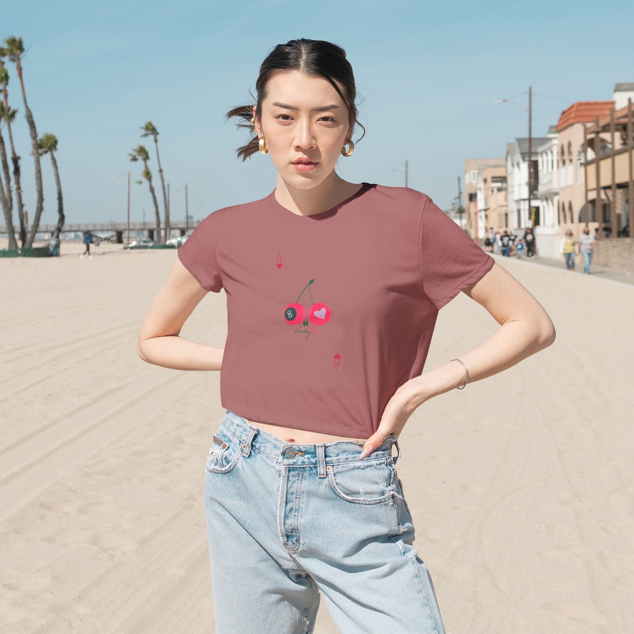 Close-up of the Lucky Me mauve cropped t-shirt, featuring cherries, heart, and ace card symbols, styled with high-waist denim.