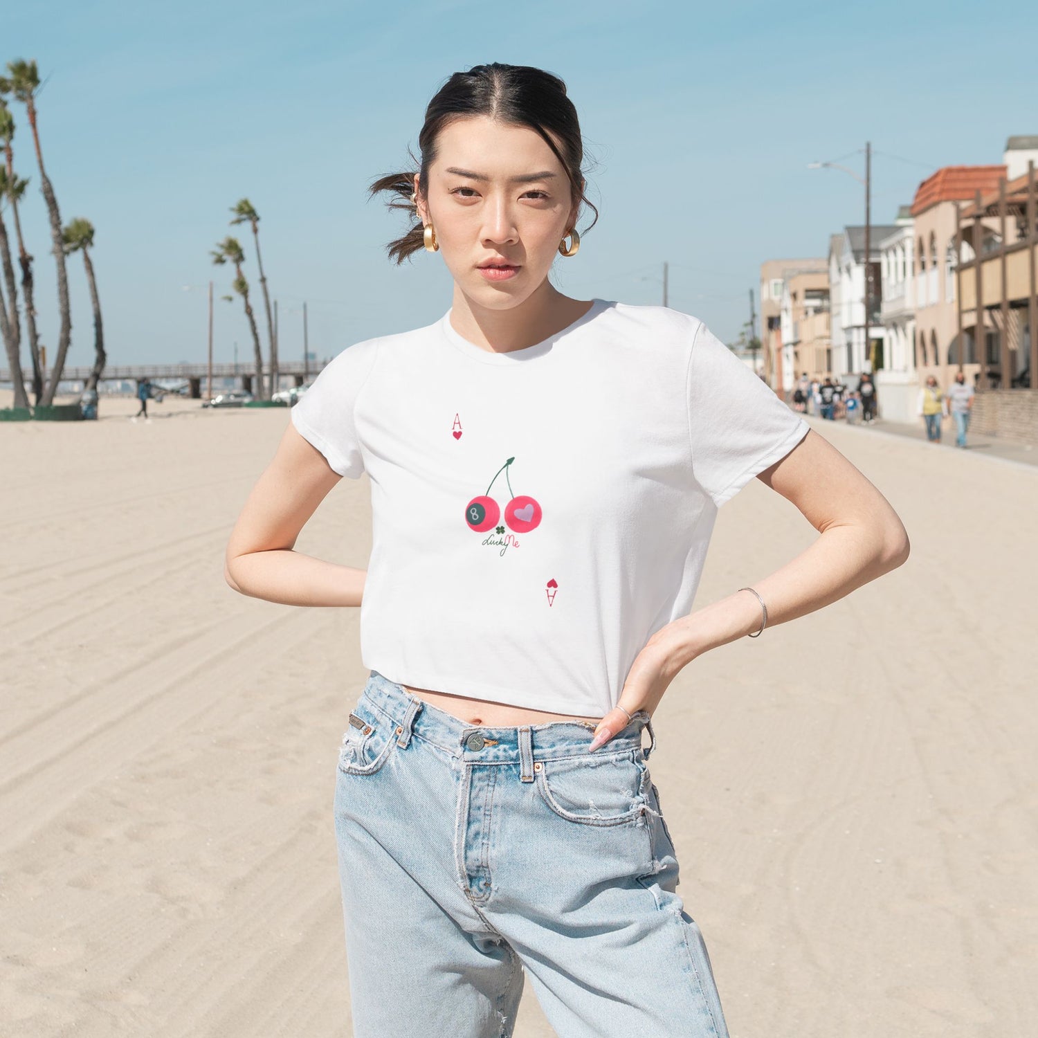 oman wearing the white Lucky Me cropped tee with cherry and 8-ball print, styled with jeans at the beach.